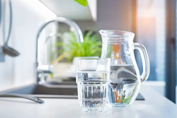 A kettle and a small glass of water on a kitchen counter at sunrise